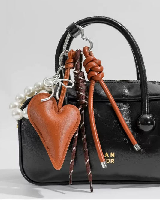 Black handbag with brown heart-shaped keychain and decorative elements on a light gray background